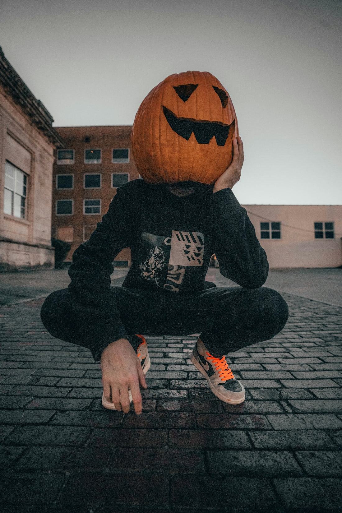 man in black jack o lantern hoodie and black pants sitting on gray brick floor during